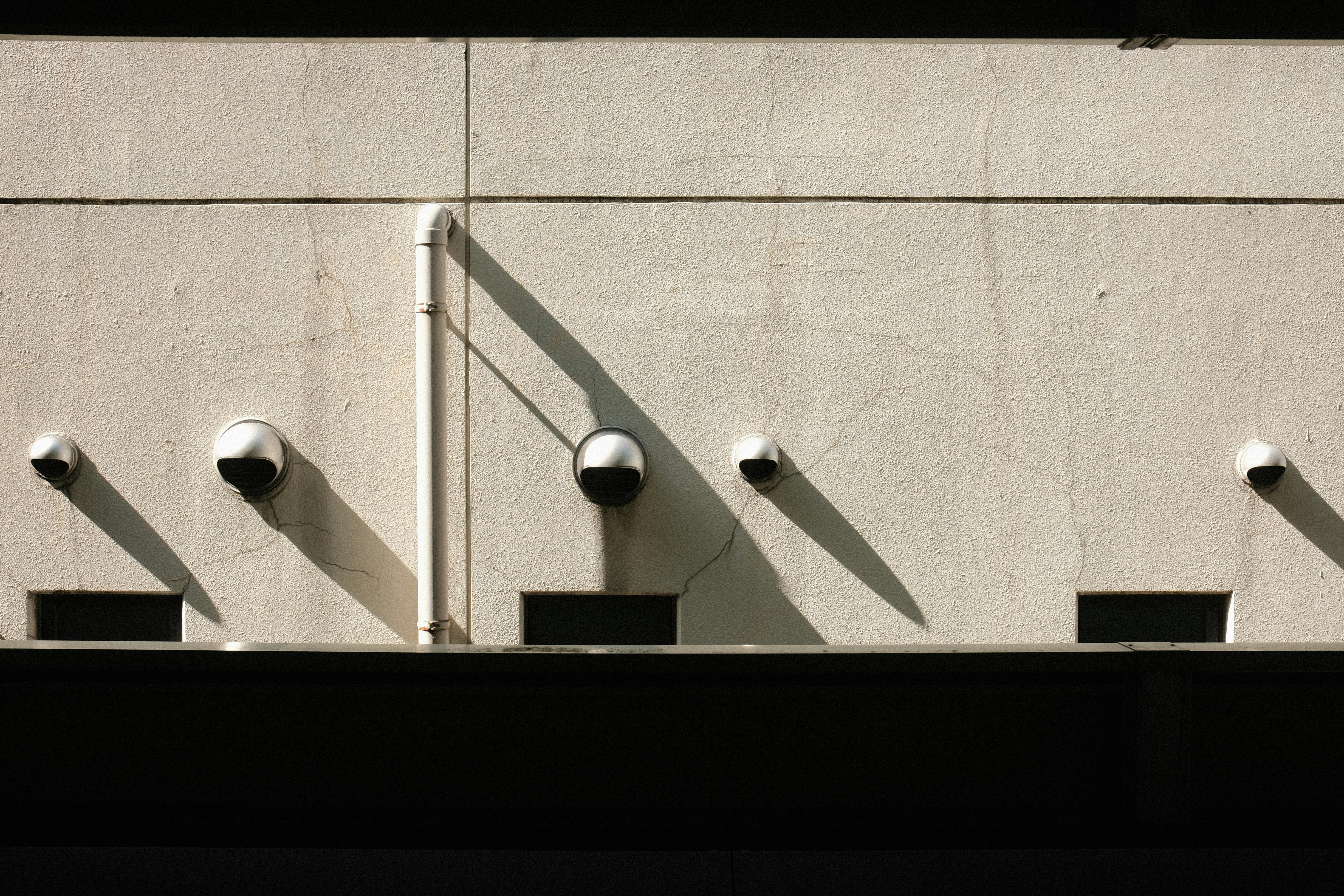 gratis Een minimalistische muur met meerdere beveiligingscamera's die lange schaduwen werpen in het zonlicht. Stockfoto