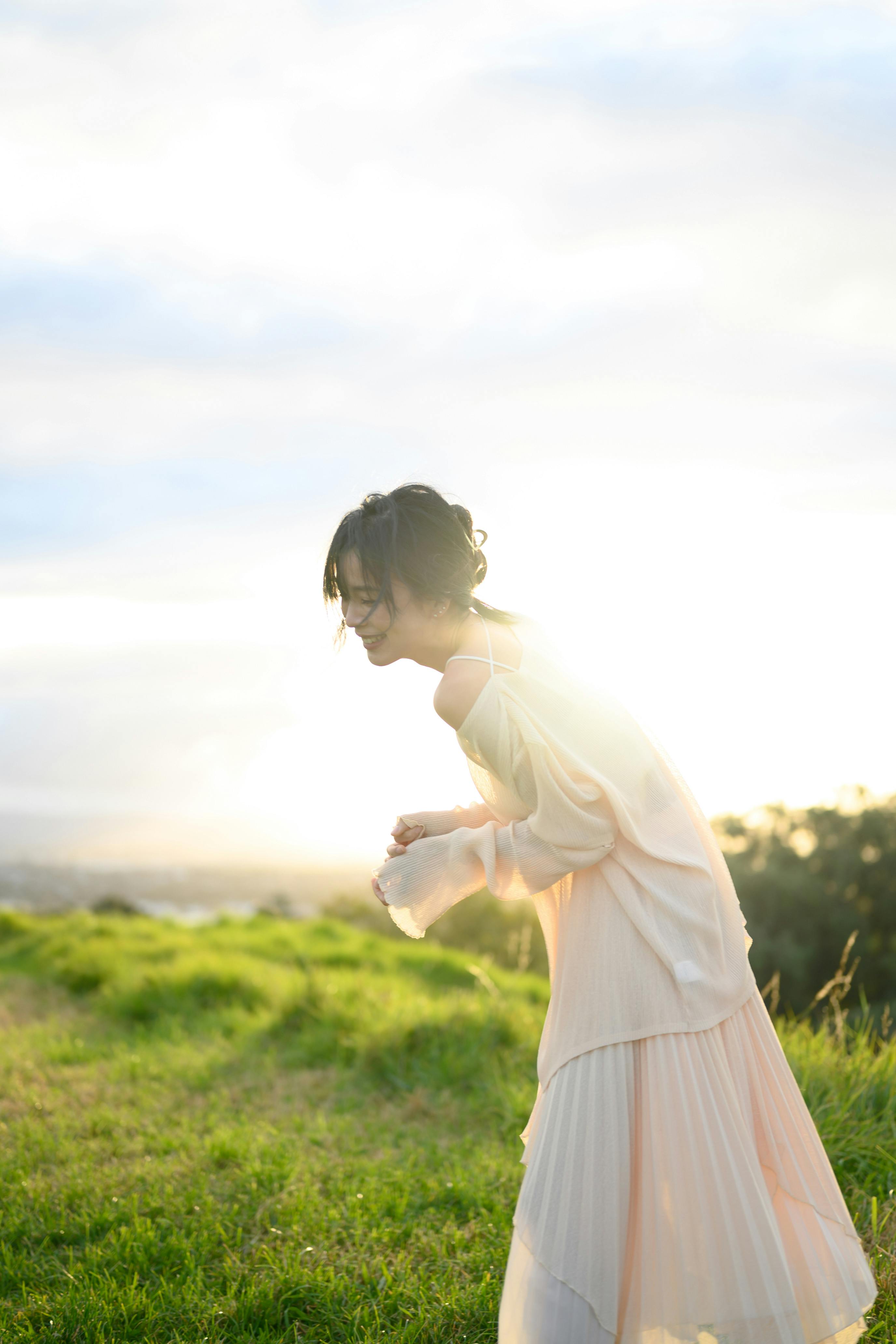 Laughing woman in a flowing dress in a sunny field, embracing nature.