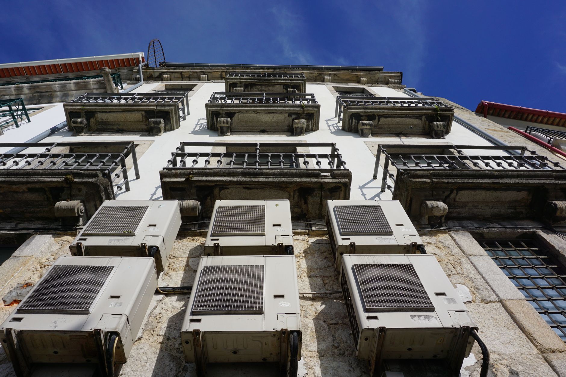 A upward view of a building facade with air conditioners and balconies in Porto.