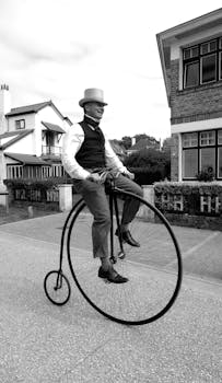 A man wearing vintage attire rides a penny-farthing bicycle on a quaint street in La Panne, Belgium.
