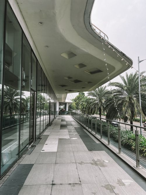 Free A modern walkway with a glass facade and palm trees lining the path, providing a serene urban escape. Stock Photo