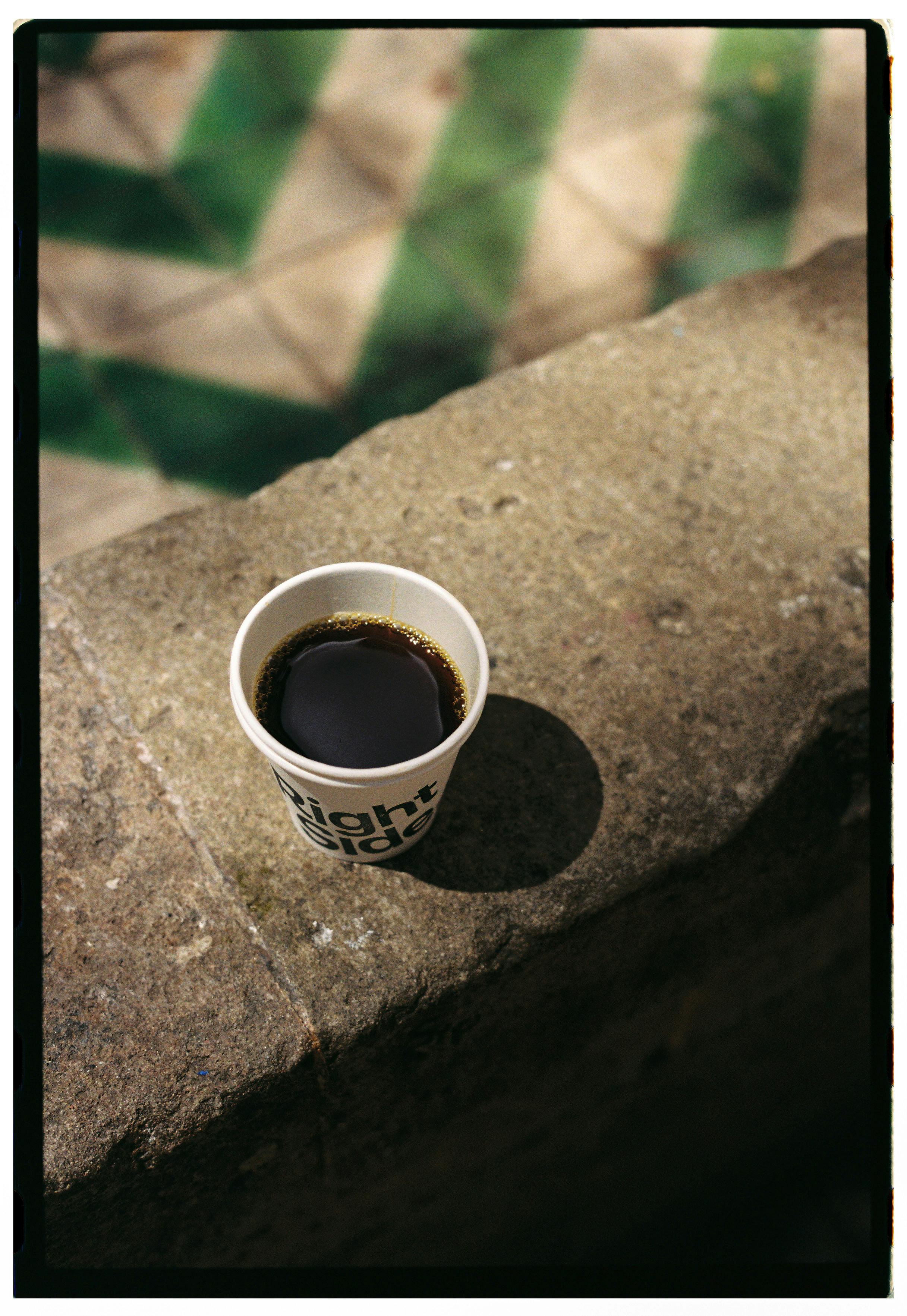 Disposable coffee cup sitting on a stone ledge under sunlight, creating a casual outdoor ambiance.