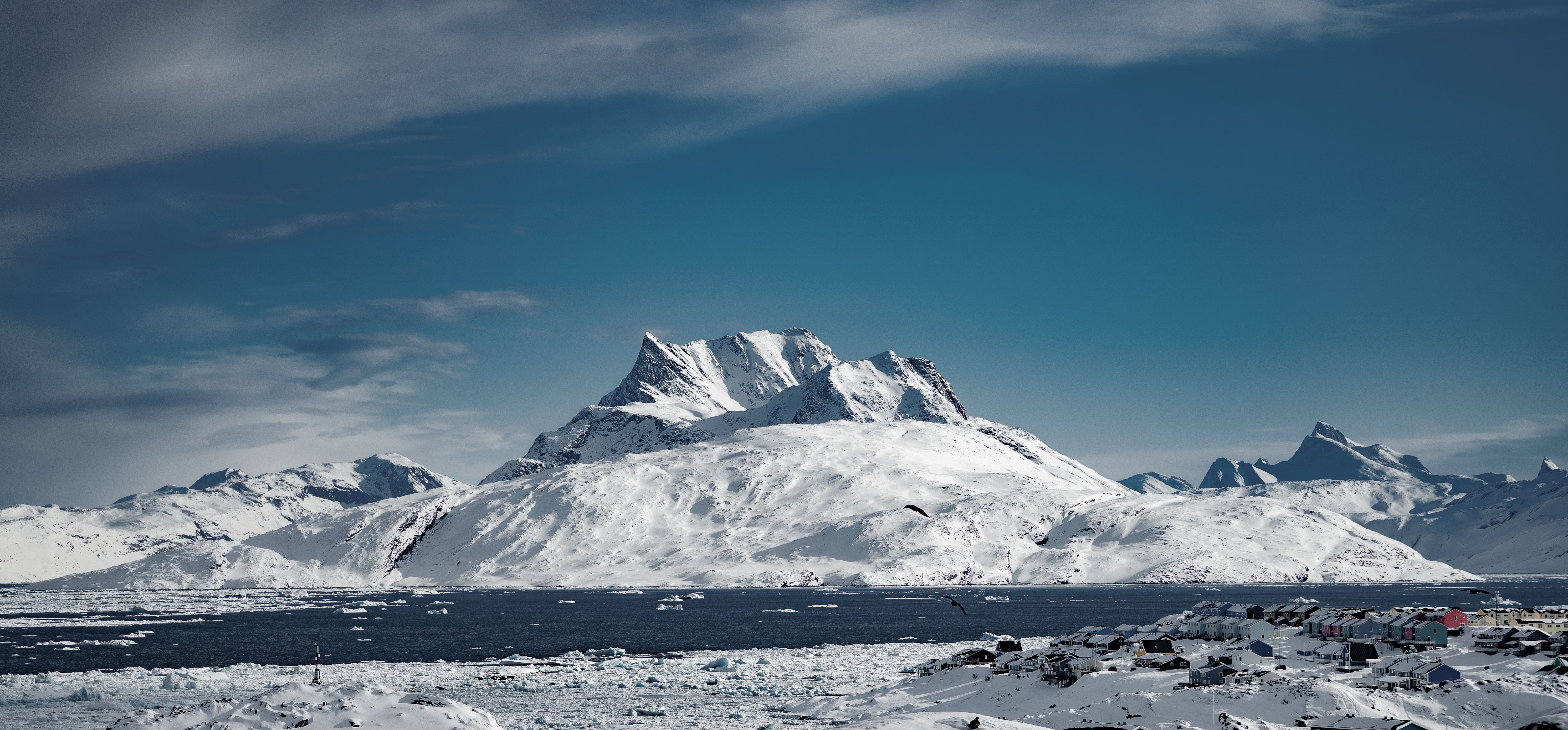 Breathtaking view of snowy mountains in Nuuk, Greenland surrounded by icy waters and clear blue skies.