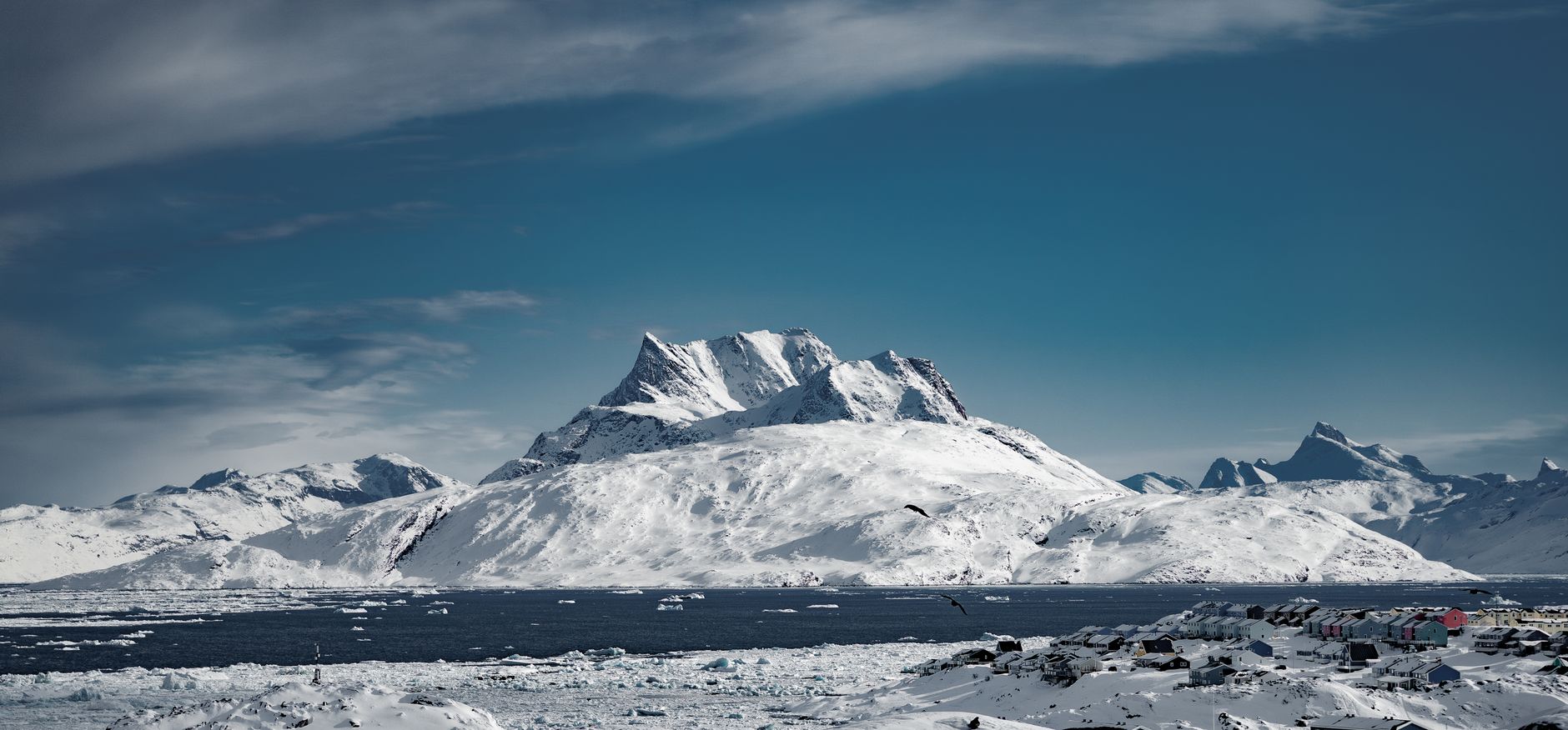 Breathtaking view of snowy mountains in Nuuk, Greenland surrounded by icy waters and clear blue skies.