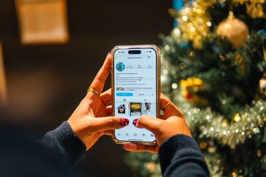 Person using a smartphone near a Christmas tree with a festive atmosphere.