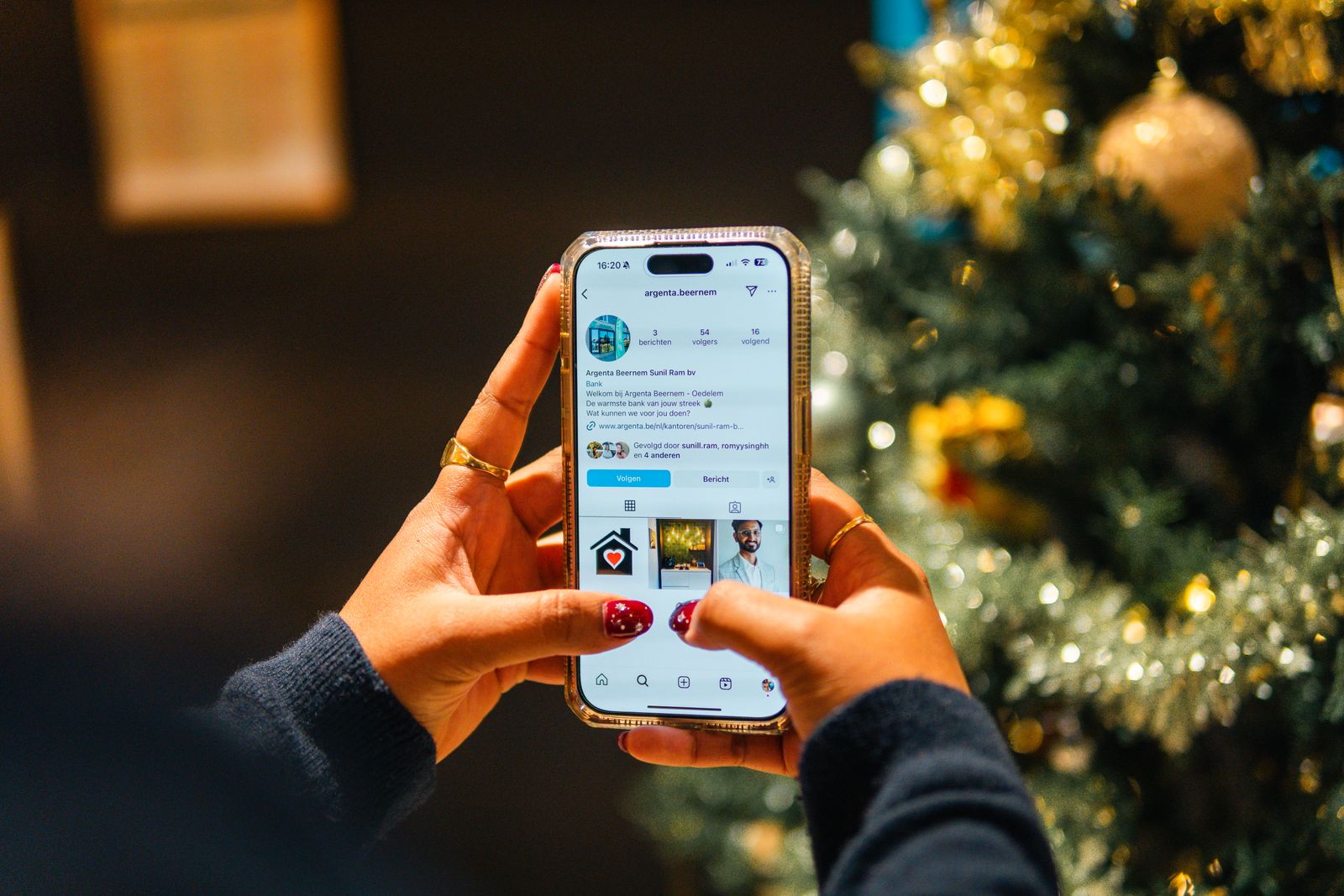 Hands using a smartphone beside a Christmas tree.