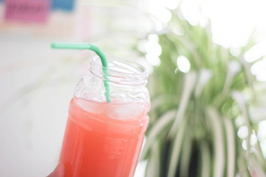 A pink drink with ice in a glass jar, featuring a green straw. Perfect summer refreshment.