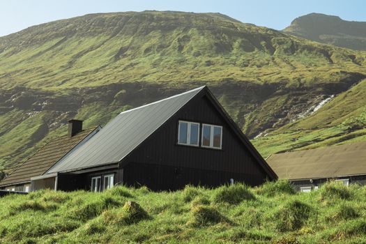 Charming black cottage nestled in lush green hills, showcasing serene mountain views.