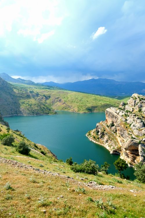 Free A breathtaking view of a mountain lake surrounded by rocky cliffs and lush greenery under a dramatic sky. Stock Photo