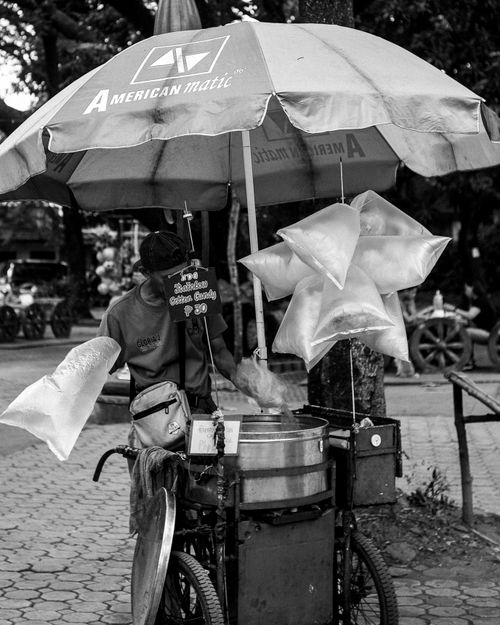 Free Black and white photo of a street vendor making cotton candy under an umbrella. Stock Photo