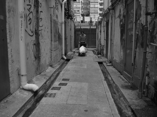 Free Black and white photo of a narrow alley in Hong Kong with person pushing cart. Stock Photo