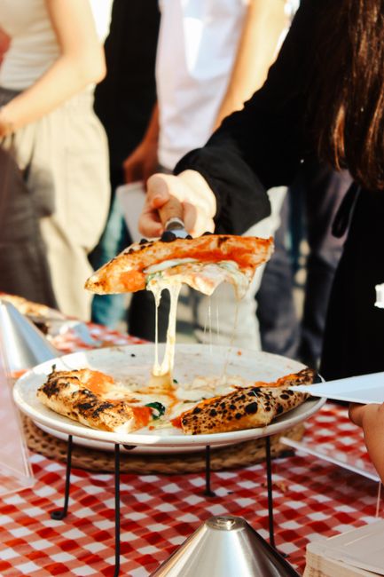 A delicious slice of pizza being served with melting cheese at an outdoor event.