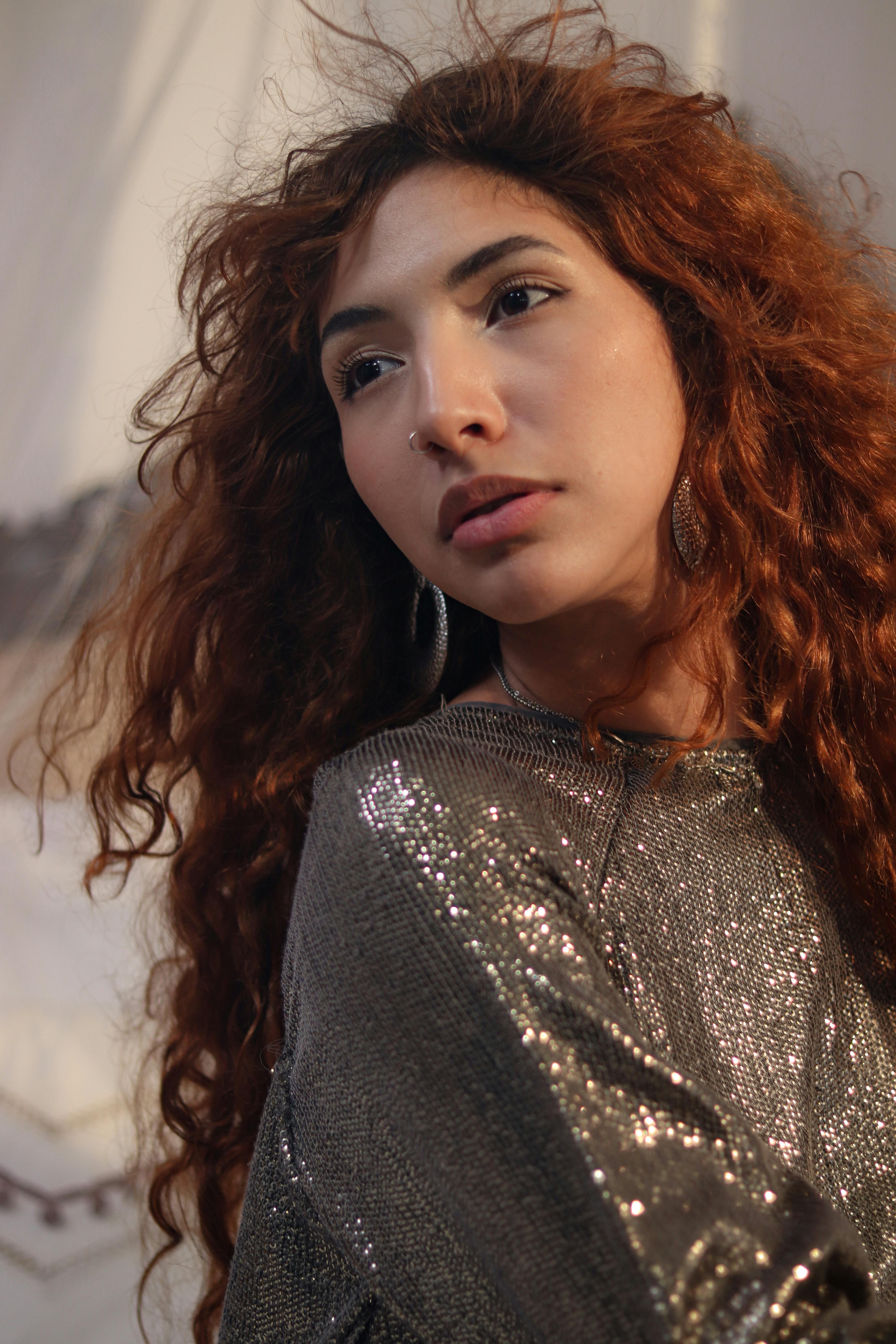 Portrait of a young woman with curly red hair and shimmering outfit.
