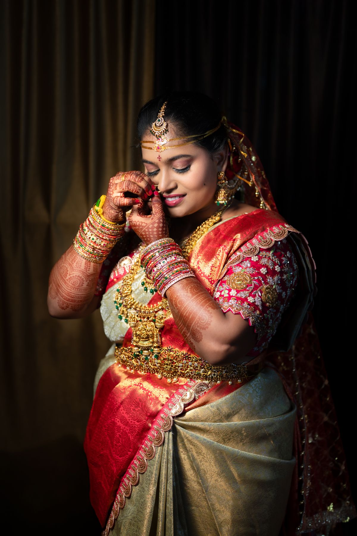 Bride in a red and gold silk saree with temple jewellery and henna, against a dark backdrop