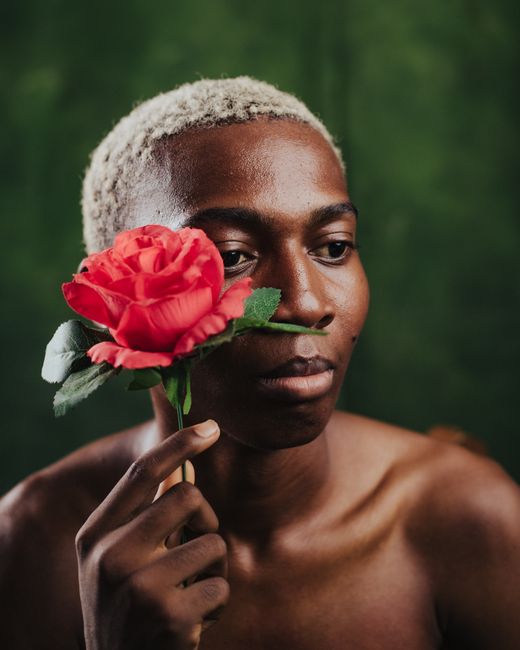 Close-up portrait of a man holding a red rose in front of a green backdrop.