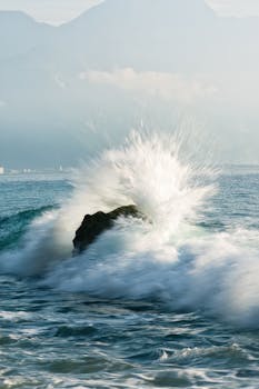 Powerful ocean waves crashing against a rock in Hualien, Taiwan, with a mountain backdrop and misty atmosphere.