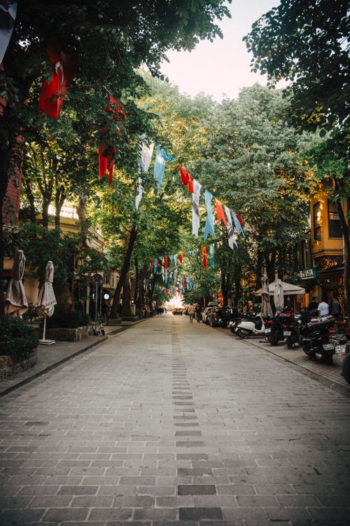 Free A tranquil street in Kuzguncuk, Istanbul adorned with colorful flags under a canopy of trees. Stock Photo