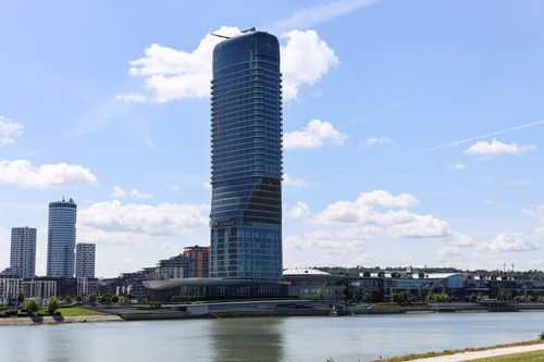 Free Impressive modern skyscraper stands tall beside a river under a clear blue sky. Stock Photo