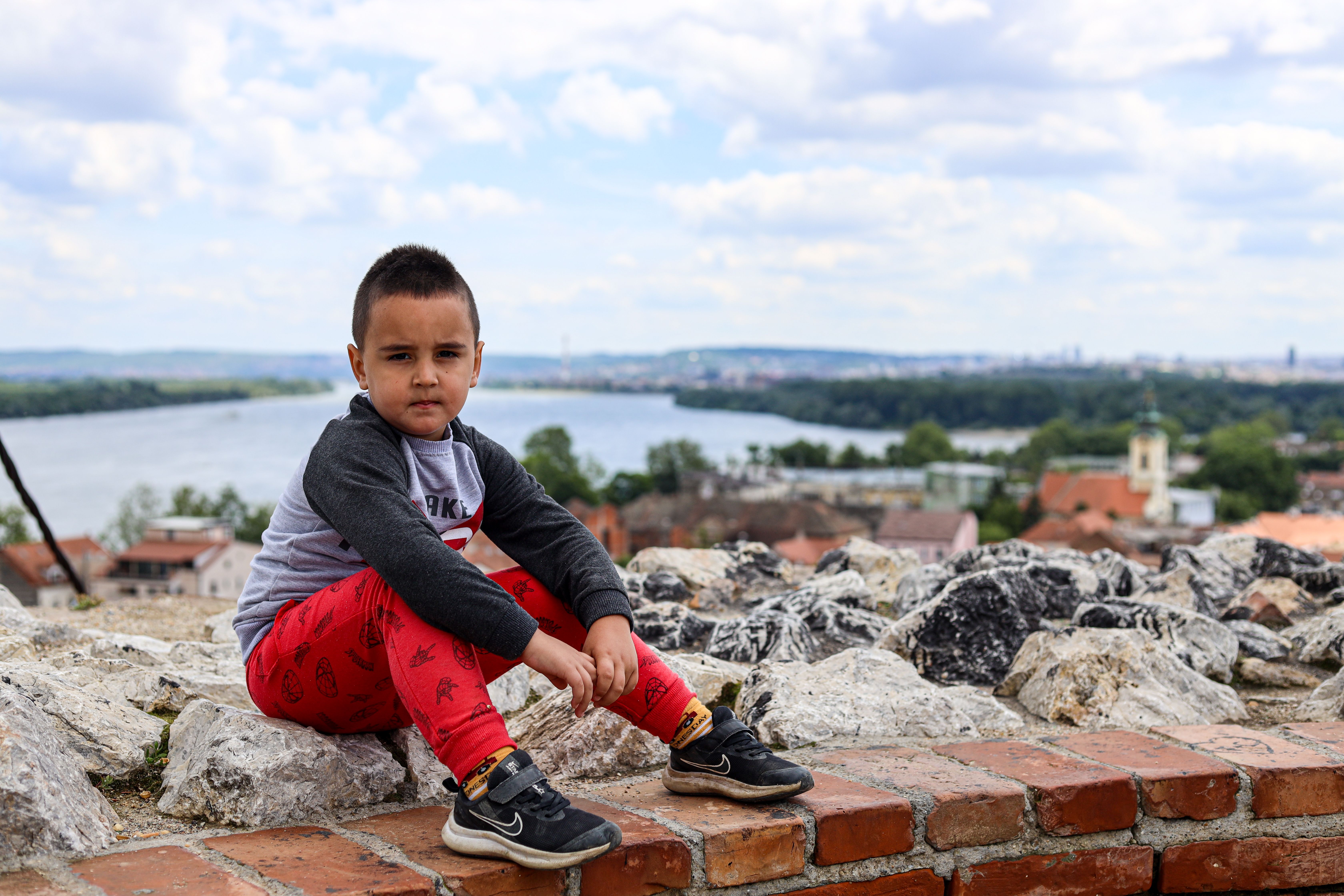 Young Boy Posing on Rustic Brick Wall by River · Free Stock Photo