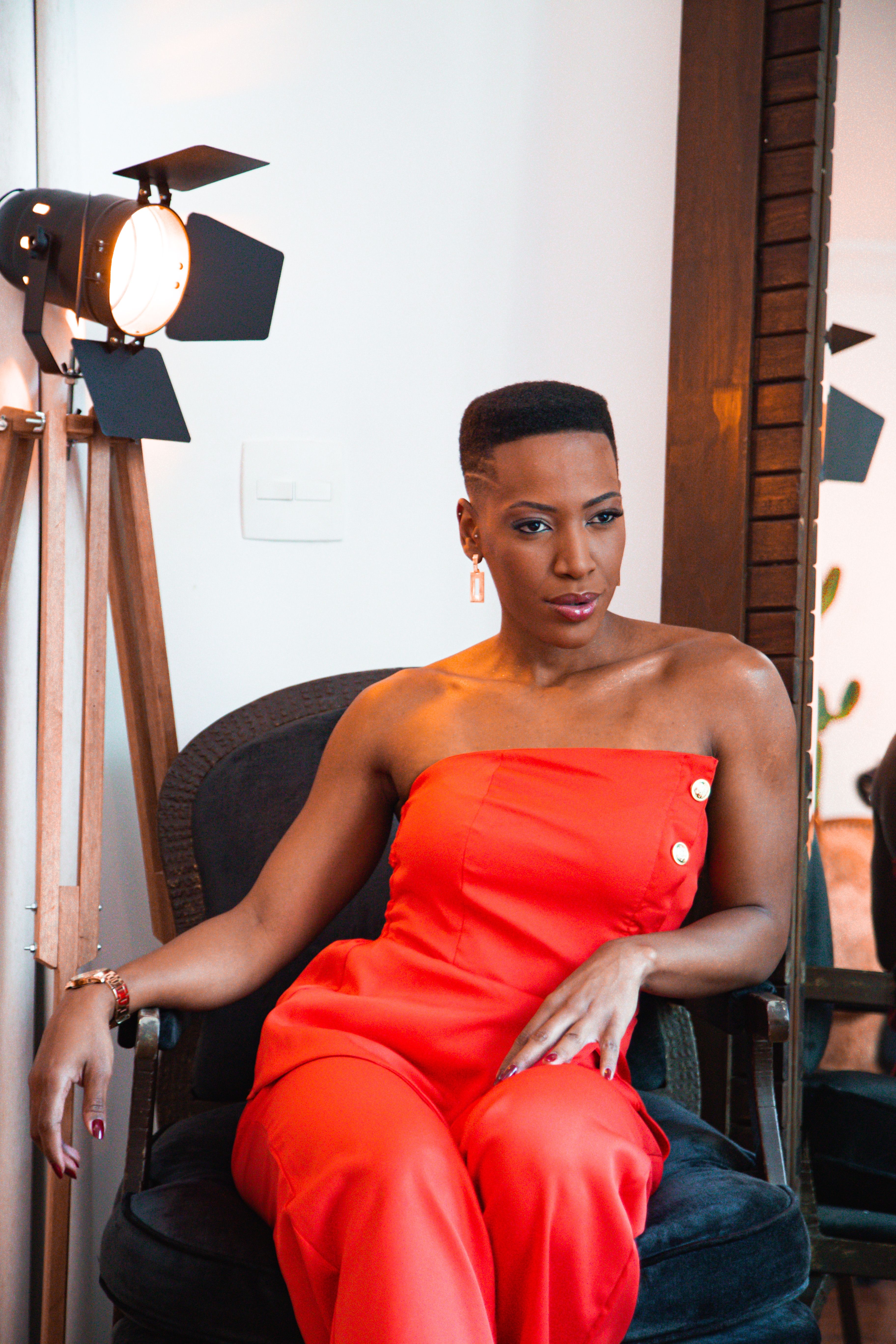 Stylish woman posing in a red jumpsuit with studio lighting indoors.