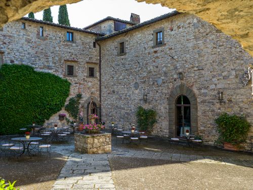 Free Rustic Italian courtyard with ivy-covered stone walls and outdoor seating. Stock Photo