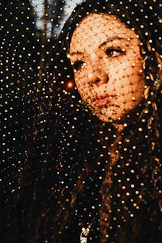 Creative portrait of a young woman with a netting shadow casting an artistic pattern on her face.