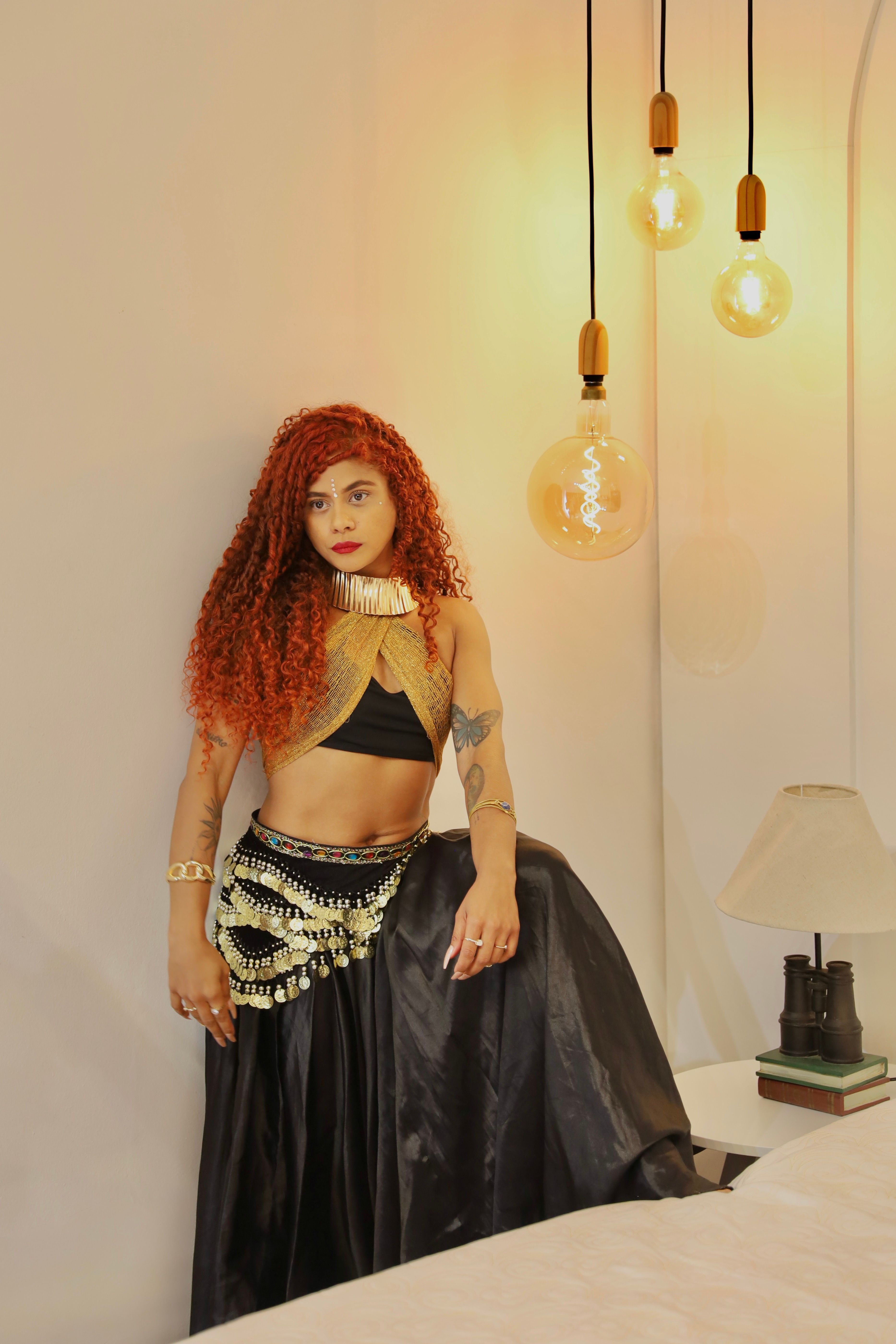 Young woman in bohemian attire posing in a modern, warmly lit room, showcasing eclectic style.