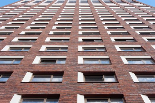 Upward view of a tall brick building facade with uniform windows against a clear sky.