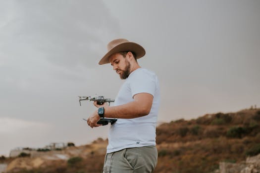 A man with a hat operating a drone outdoors during a cloudy day.