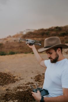 A man in a hat prepares a DJI Mavic drone for flight in a dry, desert-like landscape.