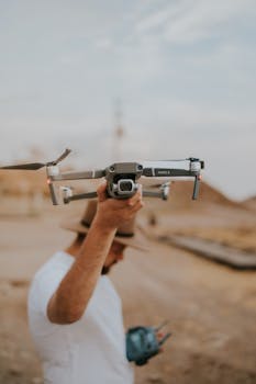 A man holds a drone in a desert landscape, showcasing modern technology and exploration.