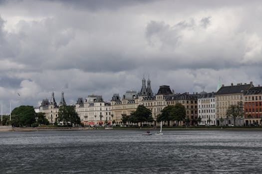 Dramatic clouds over classic Copenhagen architecture by the waterfront, showcasing elegant historical buildings.