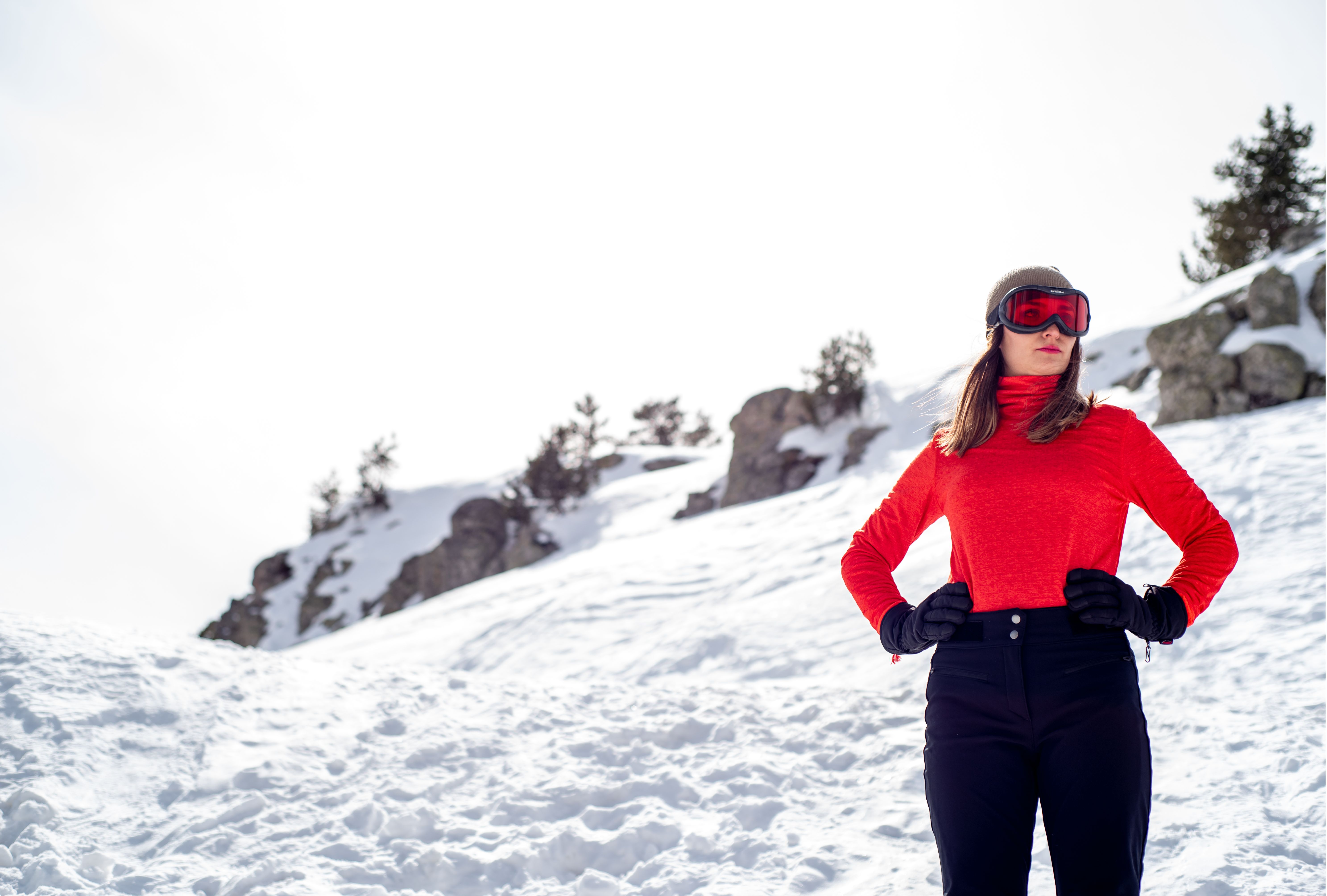 Skier in a fitted red long sleeve top and black snow pants standing on a sunny snow slope