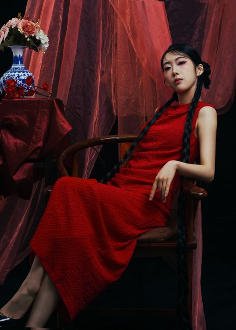 A stylish photo of a woman in a red dress sitting gracefully with long braids.