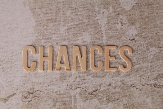 The word 'CHANCES' in wooden letters on a textured, rustic surface.