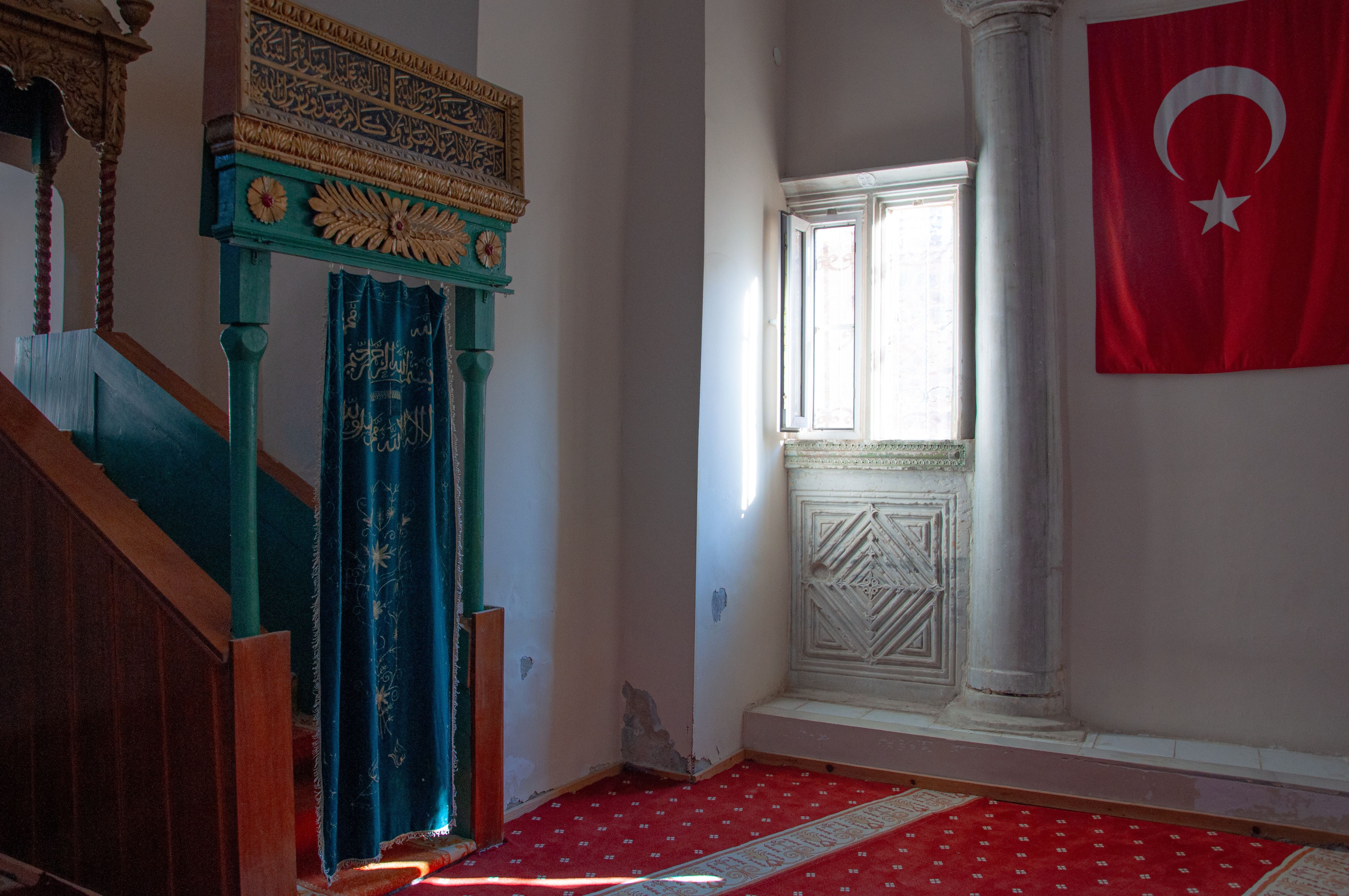 The historic interior of a mosque in Zeytinbağı, featuring traditional architecture and a Turkish flag.