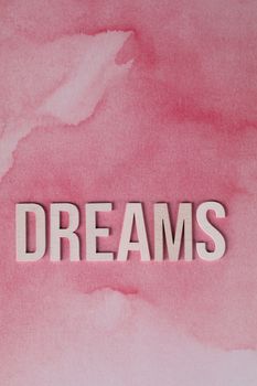Inspirational typography artwork with 'DREAMS' on a pink watercolor background, ideal for encouraging creativity.