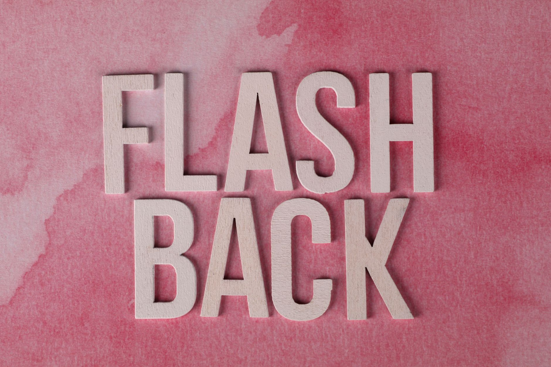 The word 'Flashback' in wooden letters on a pink watercolor background, creating a nostalgic theme.