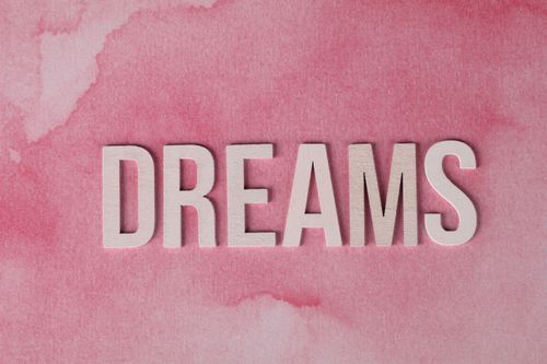 Free Inspirational 'DREAMS' text overlay on pink watercolor textured background. Stock Photo