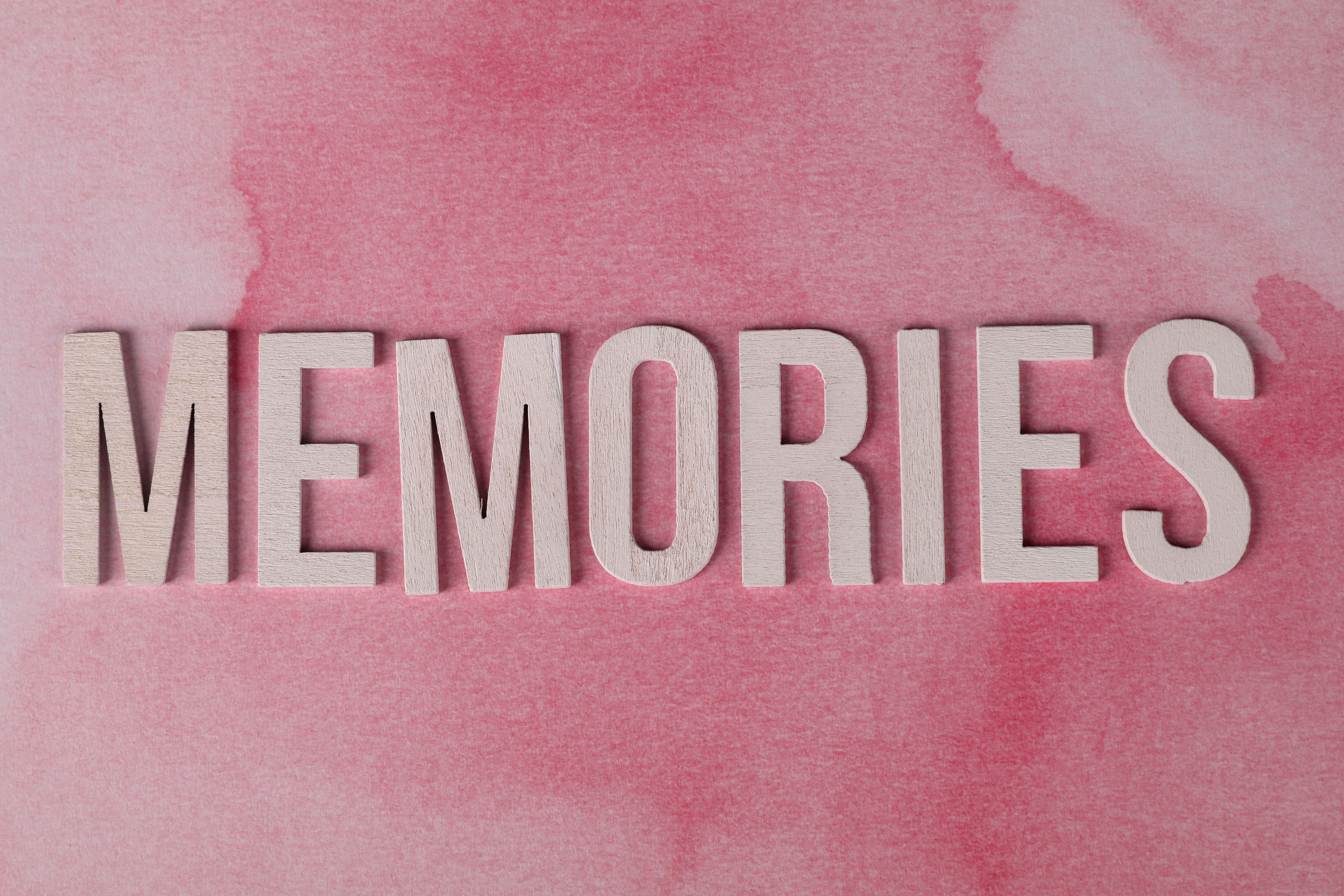 Wooden letters spelling 'Memories' on a pastel pink textured background.