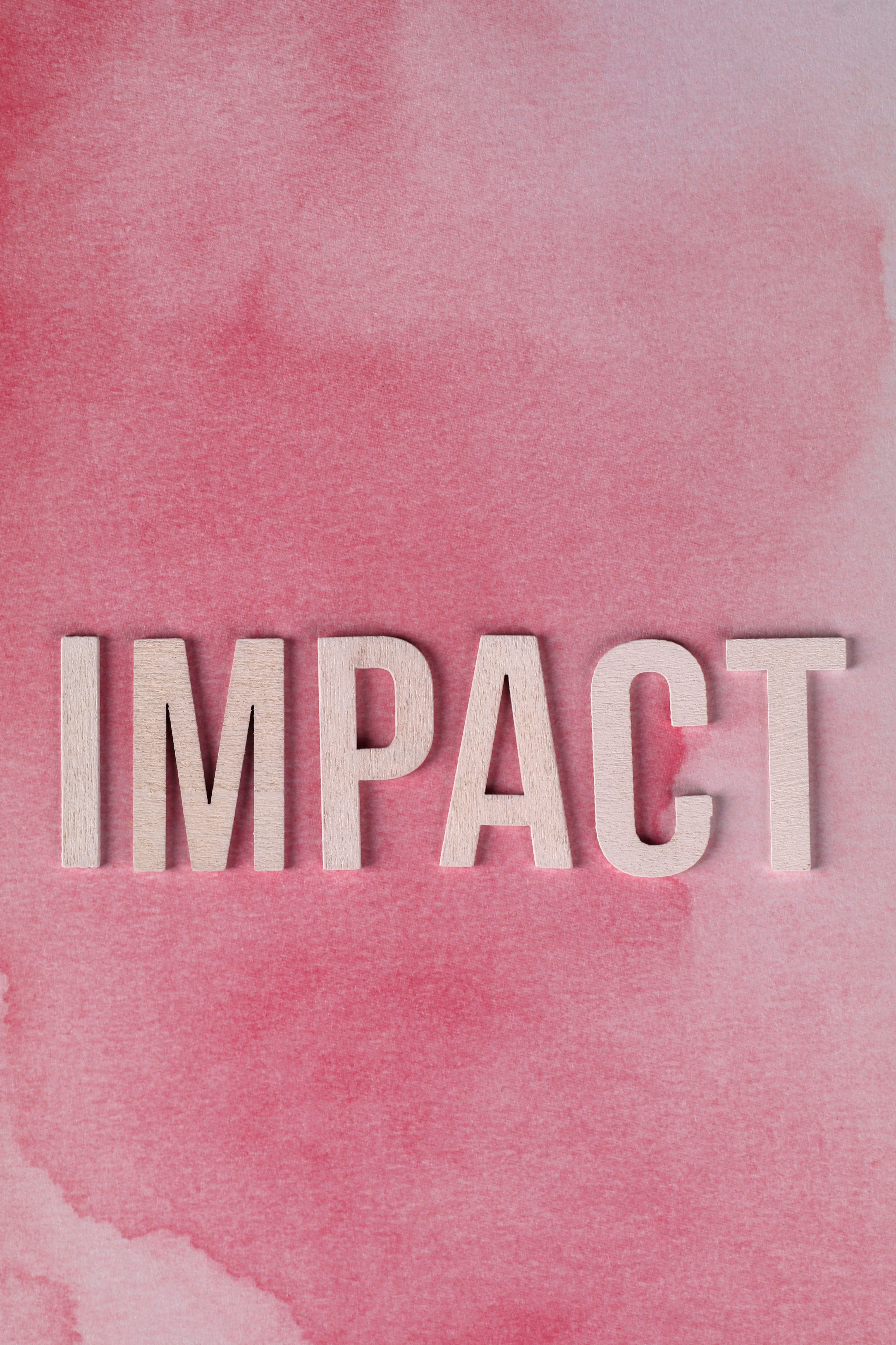 White text spelling 'IMPACT' on a pink watercolor wash evoking creativity and change.