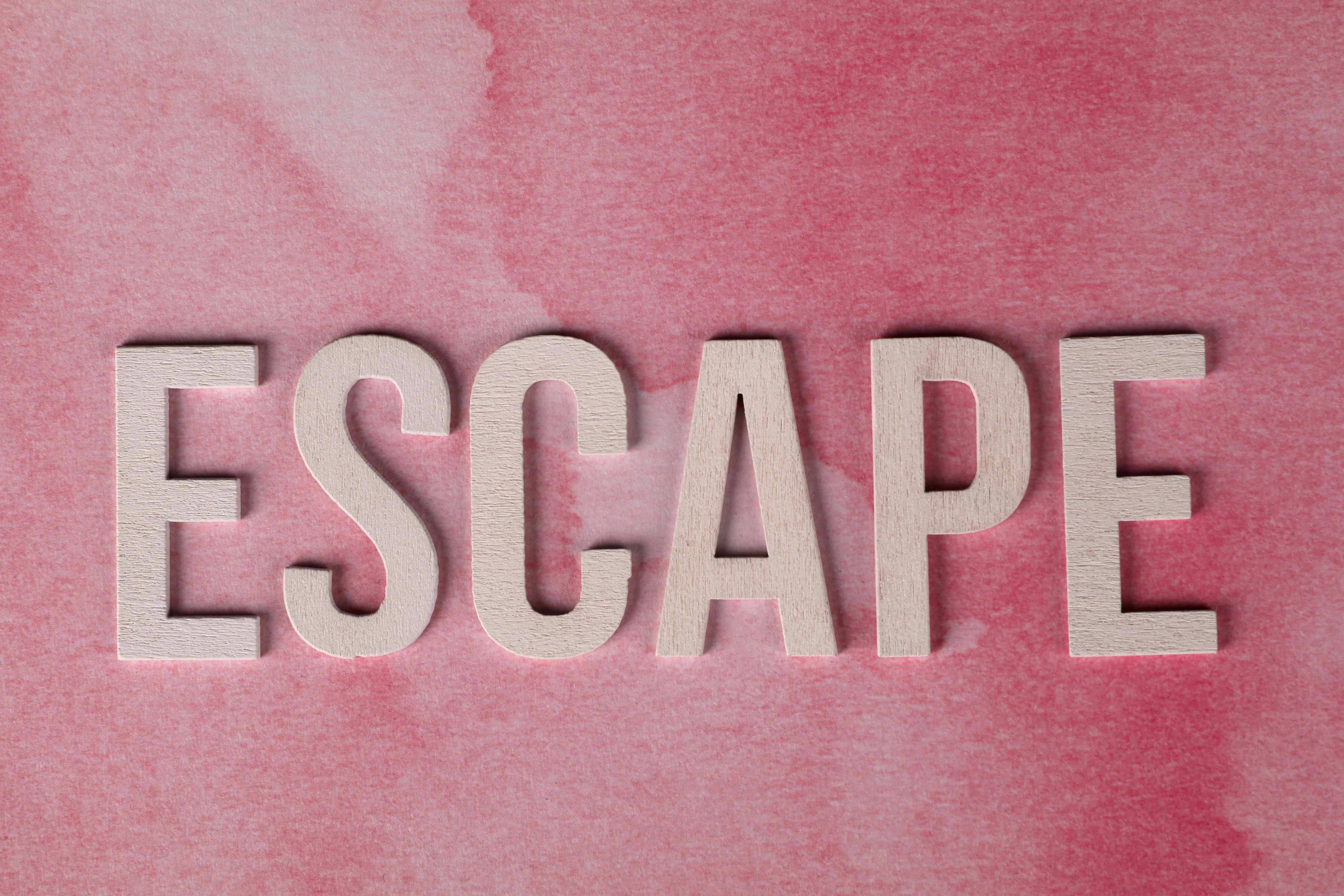 Wooden letters spell 'ESCAPE' on a pink watercolor background. Perfect for design themes.