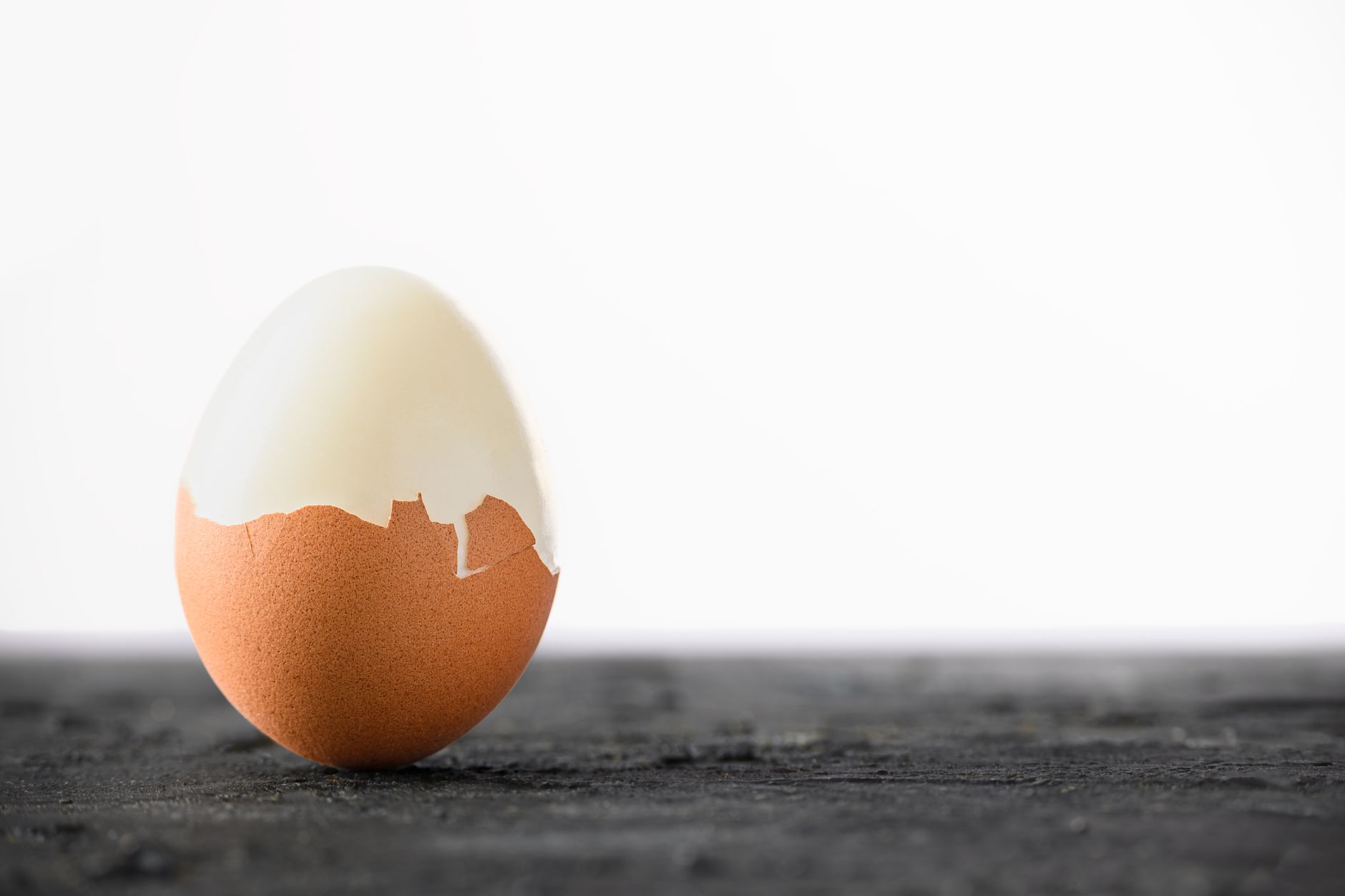 A brown boiled egg with shell partially peeled, set against a simple background.