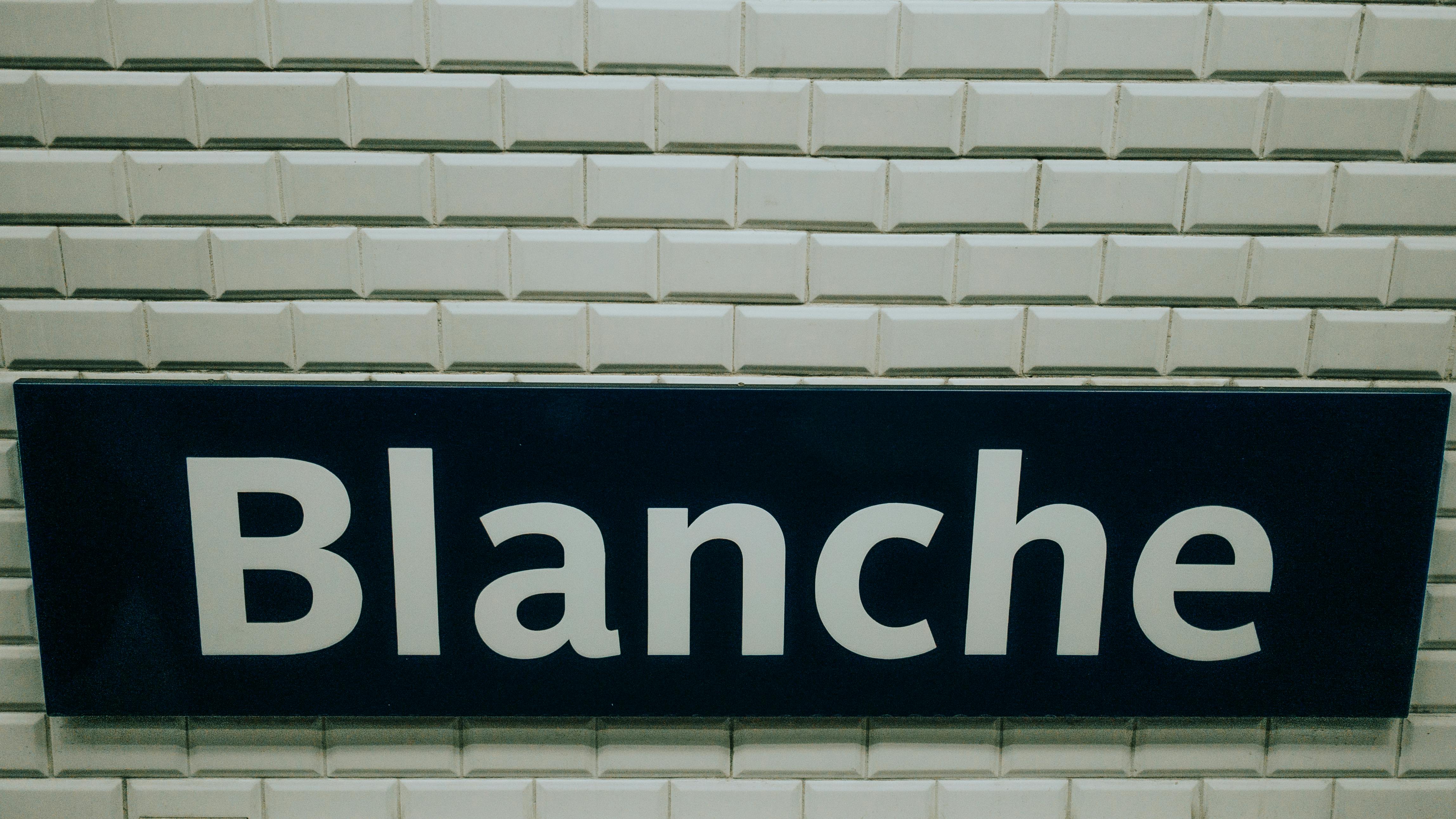 Close-up of the Blanche metro station sign in Paris, featuring white tiles and bold text.