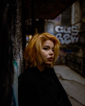 Artistic portrait of a woman in a dimly lit urban alleyway with graffiti.