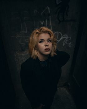 Abstract moody portrait of a woman with blonde hair in a dark urban environment.