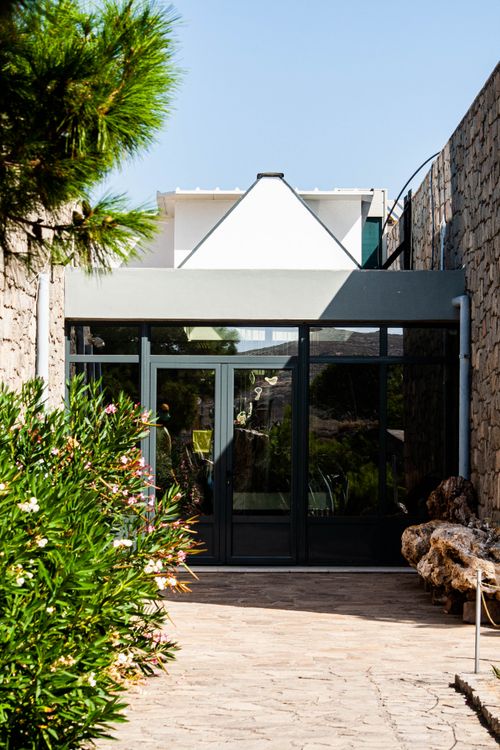 Free Minimalist glass entrance surrounded by stone walls and greenery under clear sky. Stock Photo