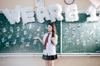 A young student in uniform celebrates graduation with decorated chalkboard backdrop.
