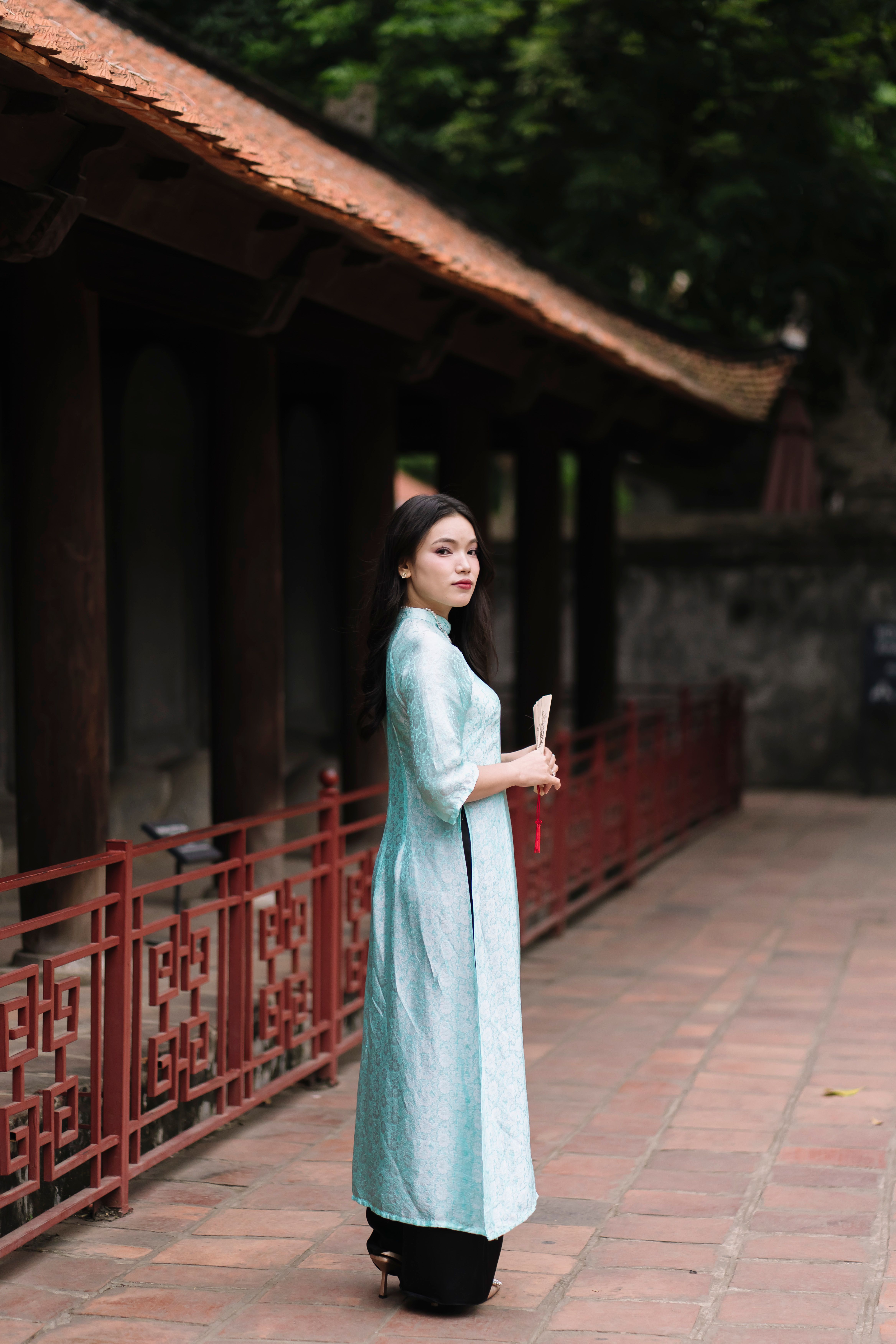 A woman in a traditional blue Ao Dai stands gracefully on a temple walkway.