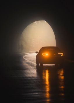 Silhouette of a car with headlights on in a foggy tunnel, creating a moody and dramatic scene.